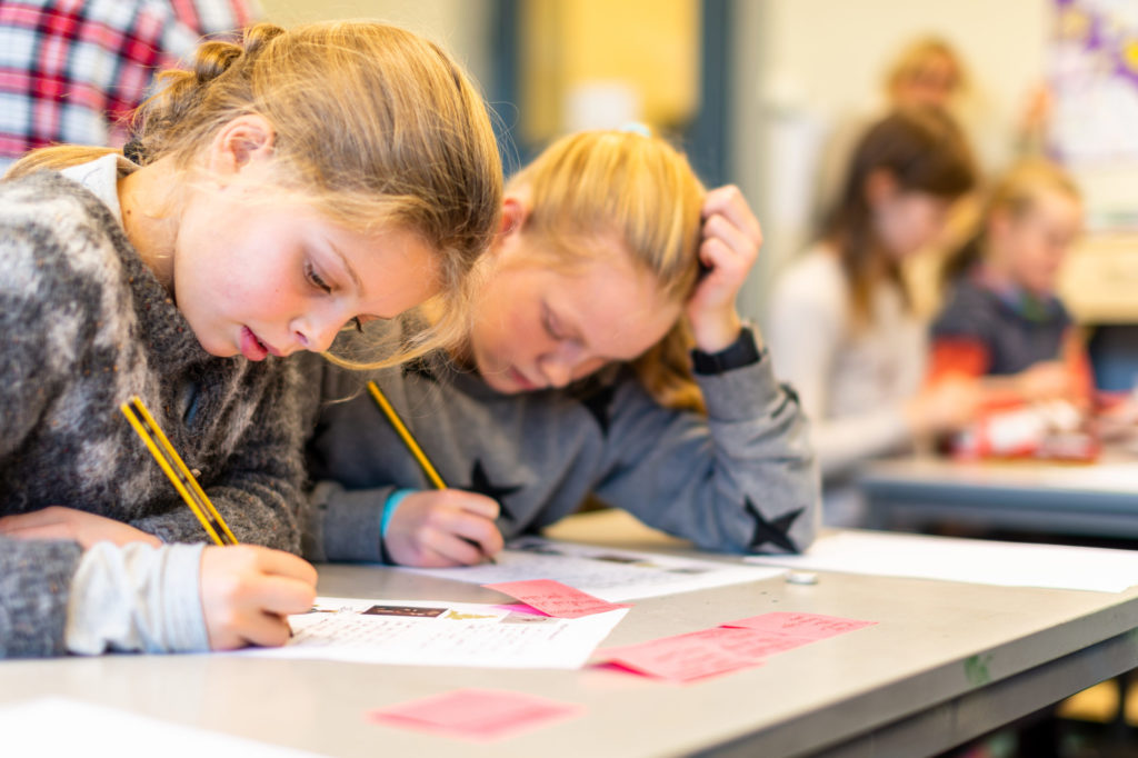 Too barneskolejenter som skriver sammendrag for hånd med hjelp av post-it-lapper.