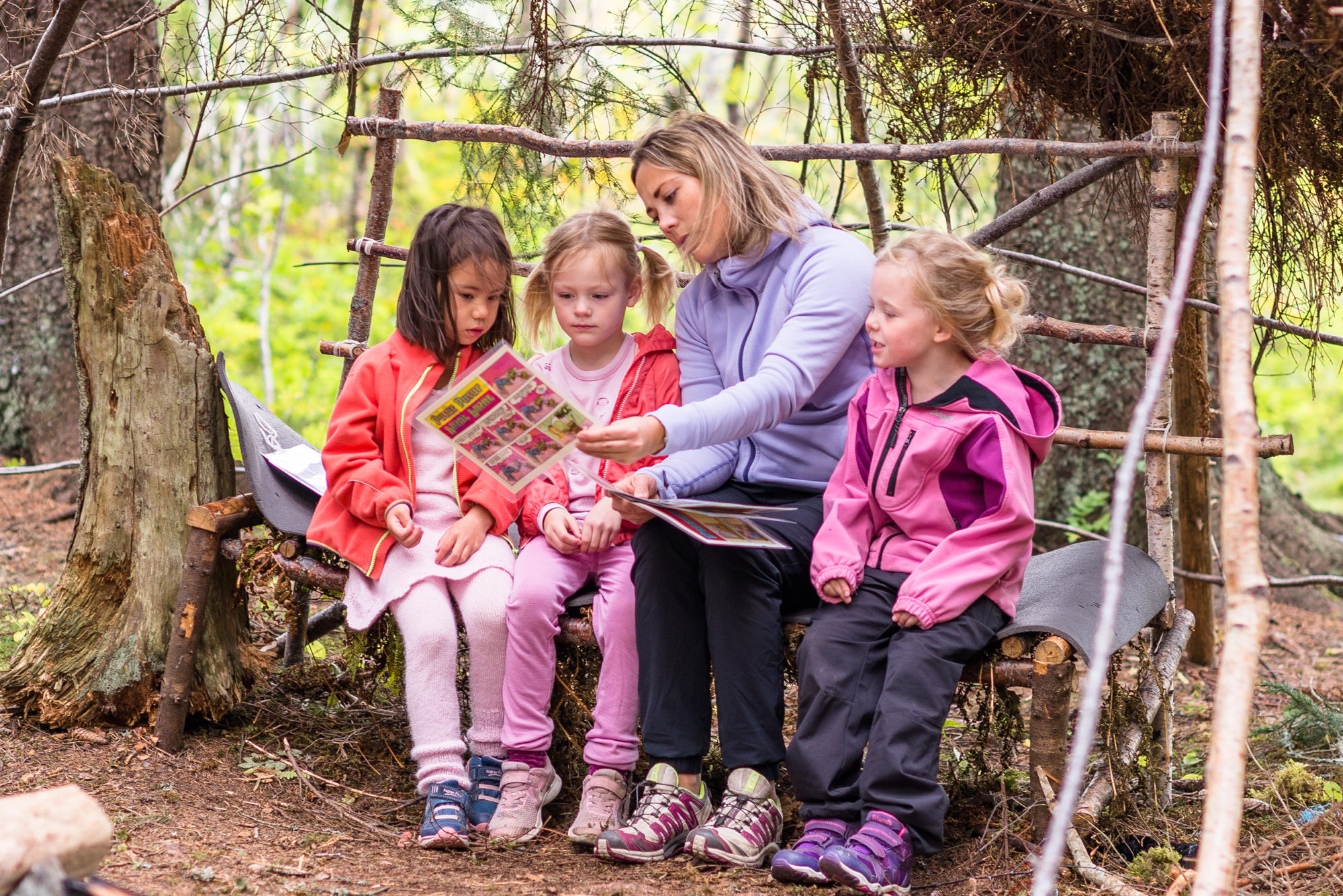 Voksen og barnehagebarn som leser tegneserie i skogen