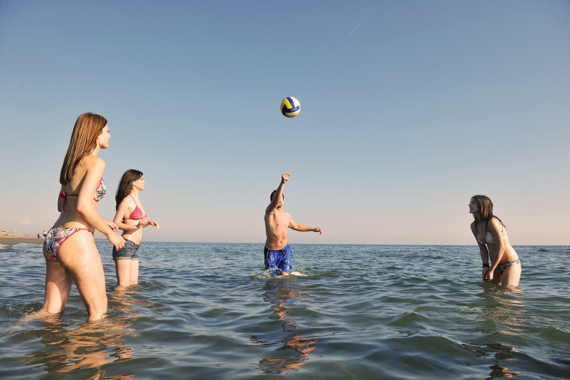 Illustrasjonsbilde av fire unge mennesker som spiller volleyball i vannet