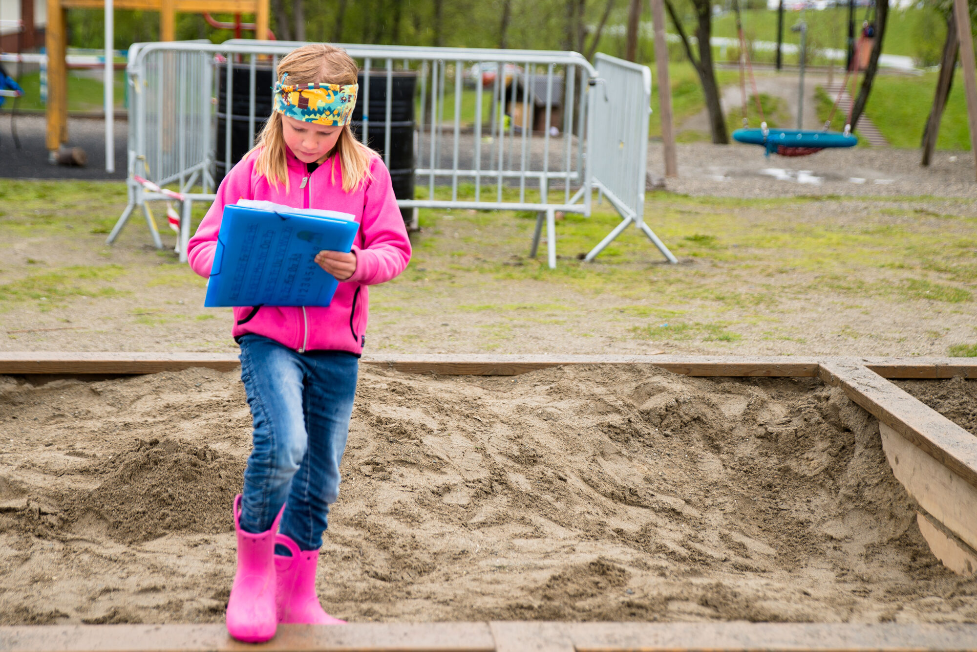 Jente på småtrinn / begynneropplæring som står og skriver i en sandkasse