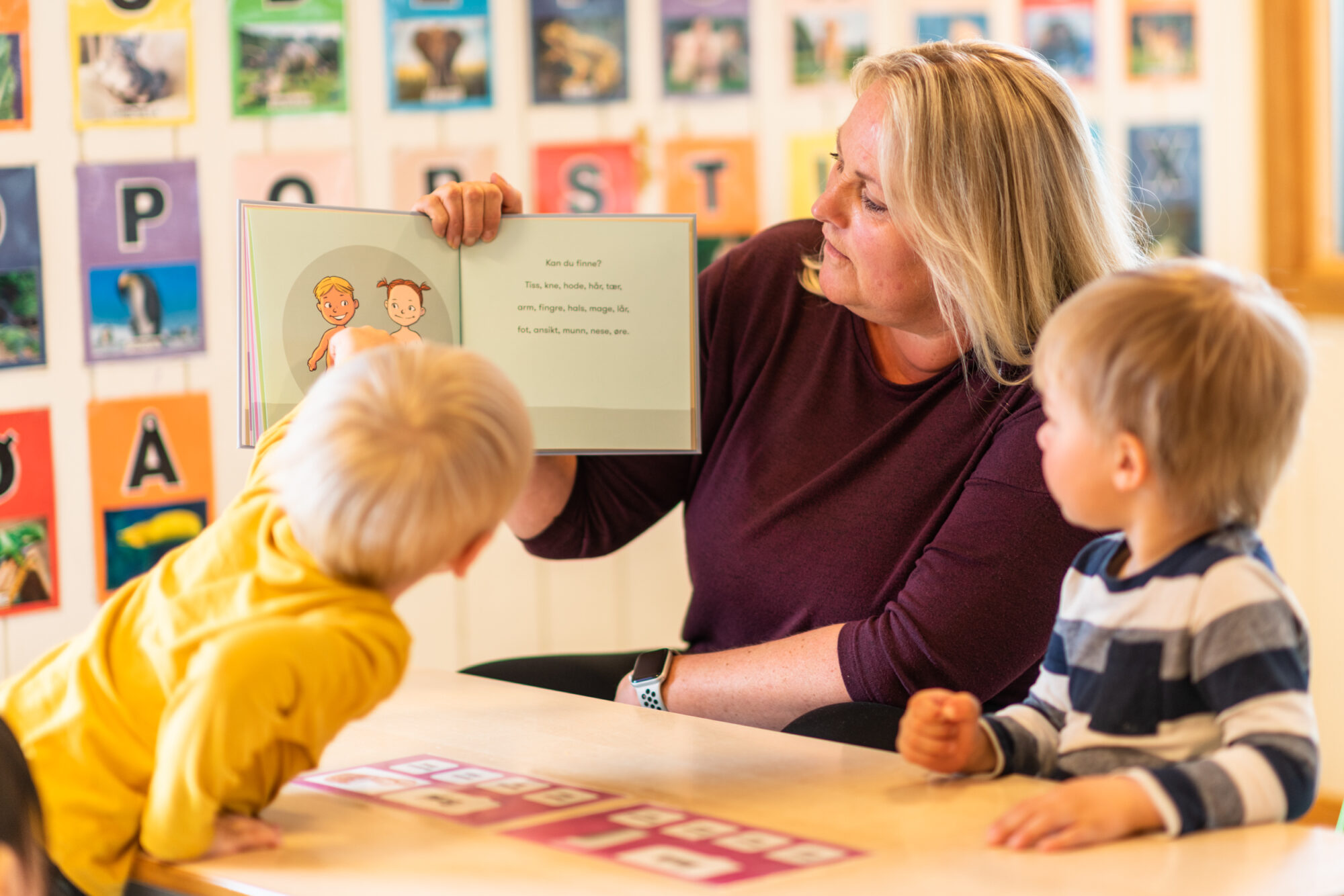 Voksen i barnehage som leser bildebok for to barn
