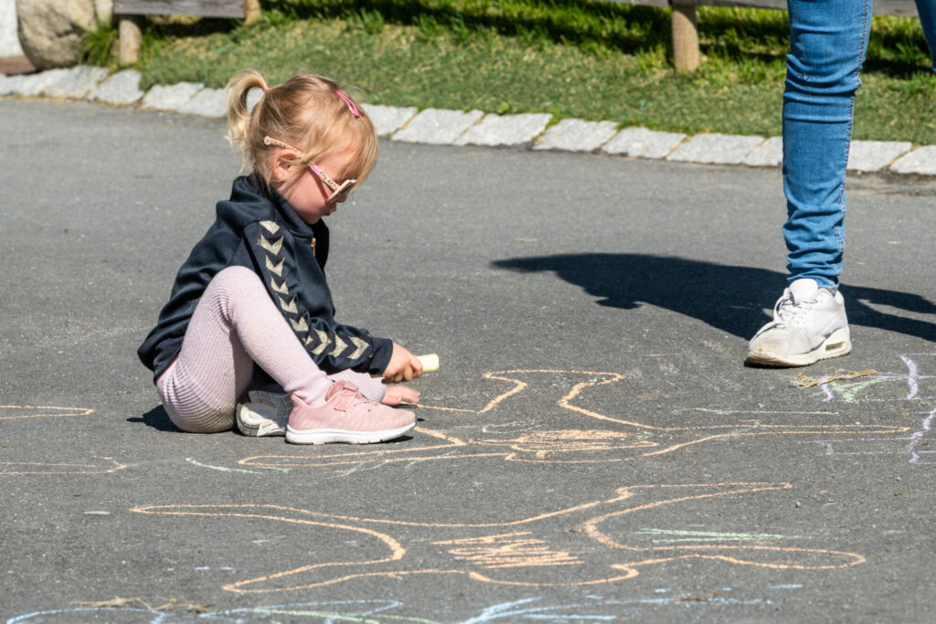 Jente i barnehagen som skriver og tegner med kritt på asfalten