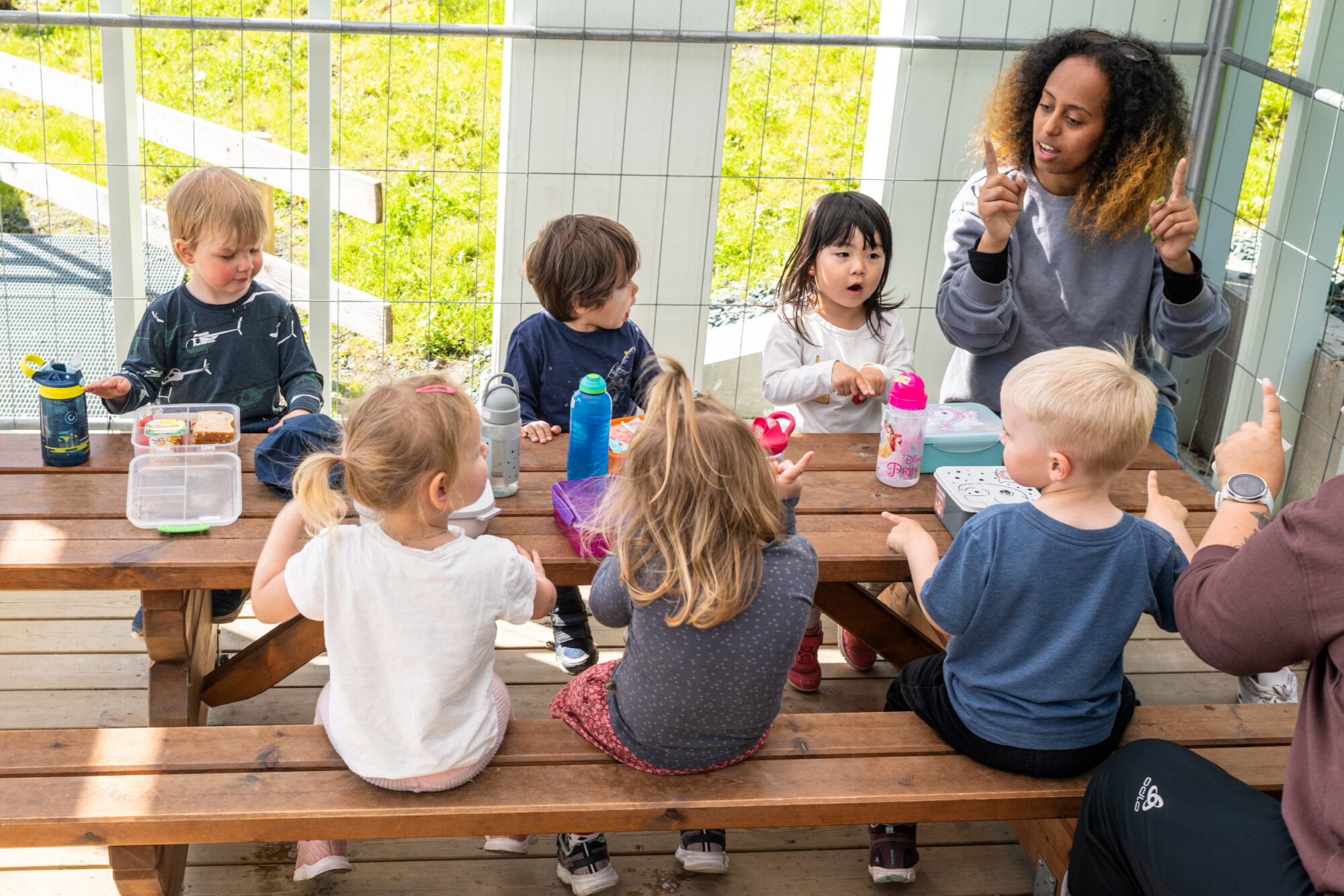 En voksen og barn i barnehagen som spiser ute