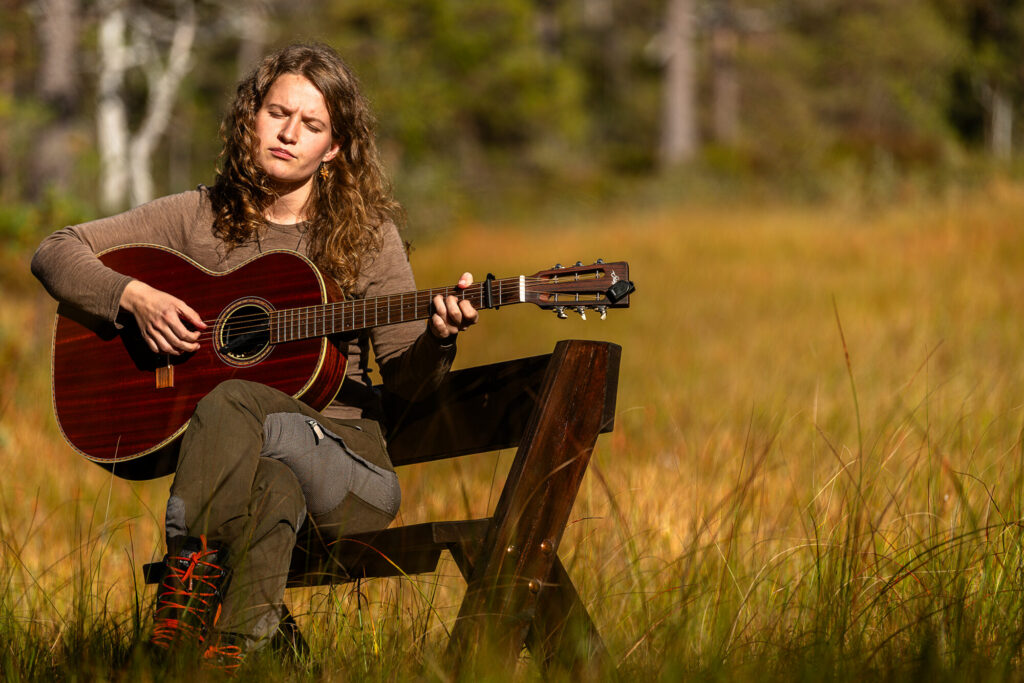 Artist Stine Bogsveen spiller på gitar og synger ute i et høstlandskap.