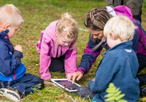 Voksen og barnehagebarn med iPad i skogen