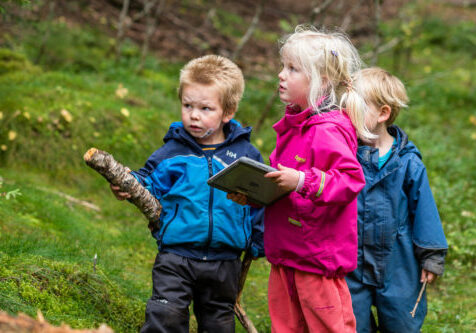 Barnehagebarn ute i naturen med iPad og pinner